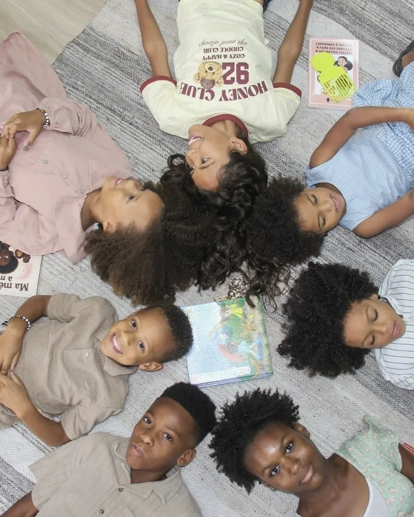 Kids with curly and coily hair lying in a circle around books